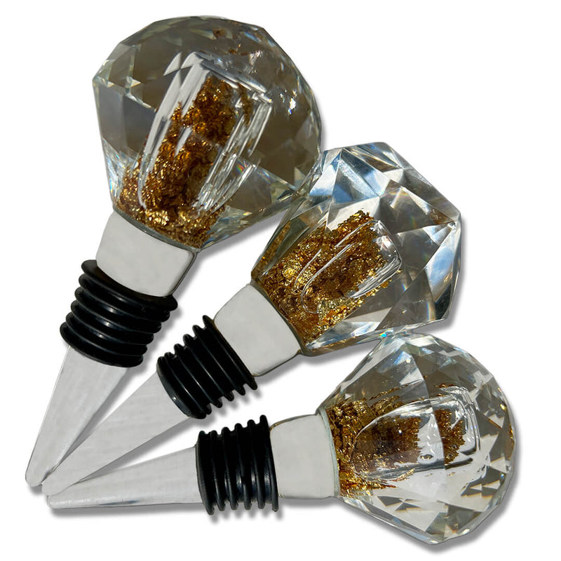 Stopper Cristal Gold Johnny Cooker para garrafas de vinho, com haste cônica , equipadas com anéis de vedação de silicone preto. Topos em material transparente facetado (nos formatos diamante e gota), revelando em seu interior um preenchimento denso de folhas douradas brilhantes.