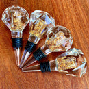 Stopper Cristal Gold Johnny Cooker para garrafas de vinho, com haste cônica , equipadas com anéis de vedação de silicone preto. Topos em material transparente facetado (nos formatos diamante e gota), revelando em seu interior um preenchimento denso de folhas douradas brilhantes.
