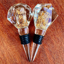 Stopper Cristal Gold Johnny Cooker para garrafas de vinho, com haste cônica , equipadas com anéis de vedação de silicone preto. Topos em material transparente facetado (nos formatos diamante e gota), revelando em seu interior um preenchimento denso de folhas douradas brilhantes.