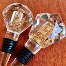 Stopper Cristal Gold Johnny Cooker para garrafas de vinho, com haste cônica , equipadas com anéis de vedação de silicone preto. Topos em material transparente facetado (nos formatos diamante e gota), revelando em seu interior um preenchimento denso de folhas douradas brilhantes.