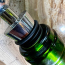 Stoppers metálicos Johnny Cooker nas cores cobre, dourado e prata, exibindo acabamento de alto brilho e anéis de silicone pretos para vedação hermética de garrafas de vinho.