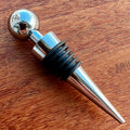 Stoppers metálicos Johnny Cooker nas cores cobre, dourado e prata, exibindo acabamento de alto brilho e anéis de silicone pretos para vedação hermética de garrafas de vinho.