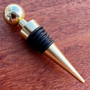 Stoppers metálicos Johnny Cooker nas cores cobre, dourado e prata, exibindo acabamento de alto brilho e anéis de silicone pretos para vedação hermética de garrafas de vinho.