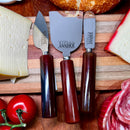 Três facas para queijos da marca Johnny Cooker com lâminas de aço inox polido (modelos lança, cutelo e espátula) e cabos cilíndricos em pedra natural Ágata polidos brilhantes.